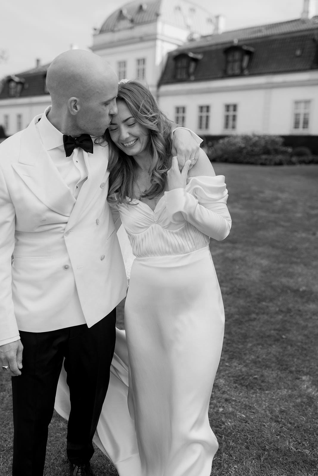 Black and white editorial wedding photo of a couple at Jordberga Slott. Captured by wedding photographer Karin Lundin. The groom wears a white Suit Supply suit, and the bride wears a Fadie El Khoury wedding dress. Planned by Freddy Wedding.