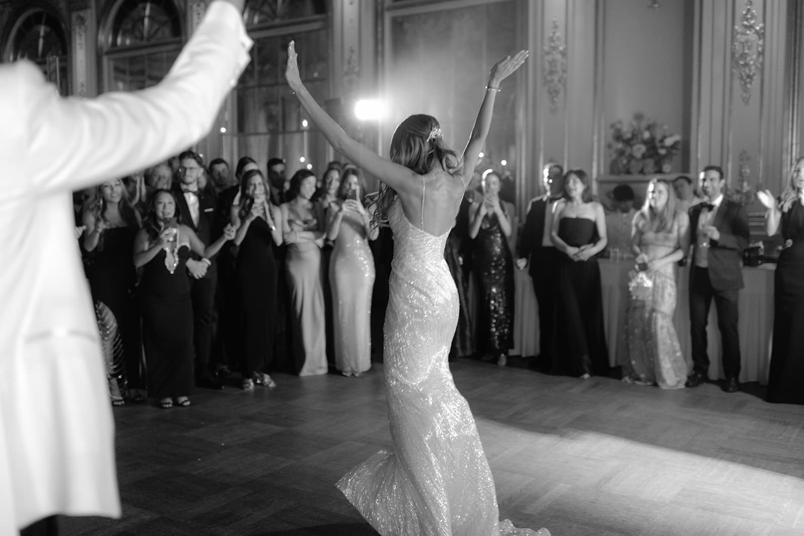 Black and white photo of a bride dancing in the Hall of Mirrors at Grand Hôtel, Stockholm. Captured by wedding photographer Karin Lundin. Guests applaud in the background as the first dance concludes. The bride wears a timeless white gown adorned with rhinestones. Planned by WeddingPlanner Stockholm.