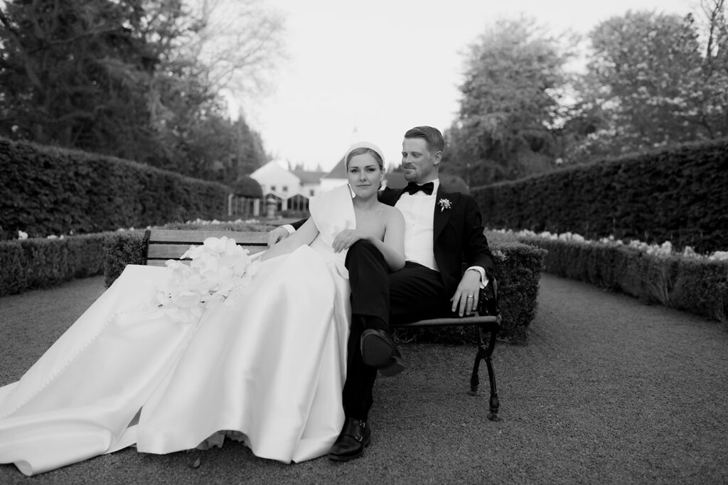 Wedding at Norrvikens trädgårdar 51 Couple posing in the hedge garden, the bride leaning against a bench with her dress draped, black and white