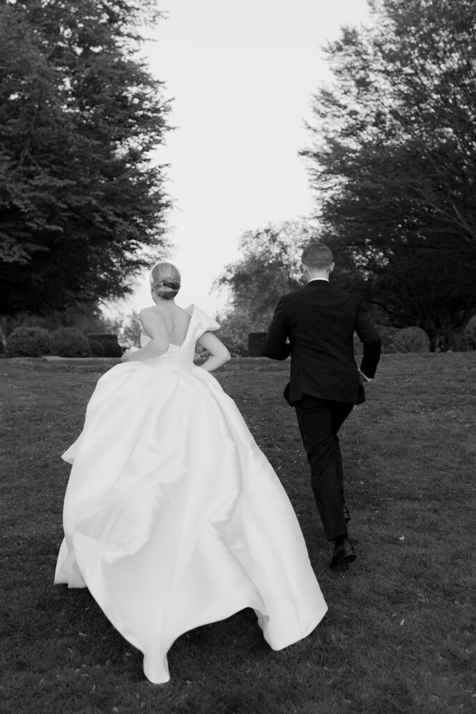 Wedding at Norrvikens trädgårdar 52 Black and white: the couple running across the lawn towards the trees