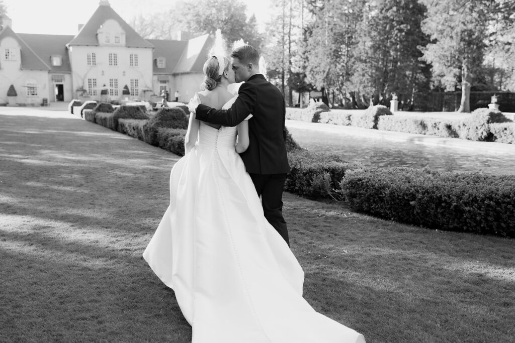 Wedding at Norrvikens trädgårdar 66 Black and white: the couple walks on the lawn towards a large white house, arm in arm