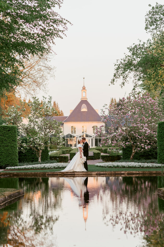 Wedding at Norrvikens trädgårdar 67 The couple reflected in the pond in front of Villa Abelin in evening light, tall hedges on both sides