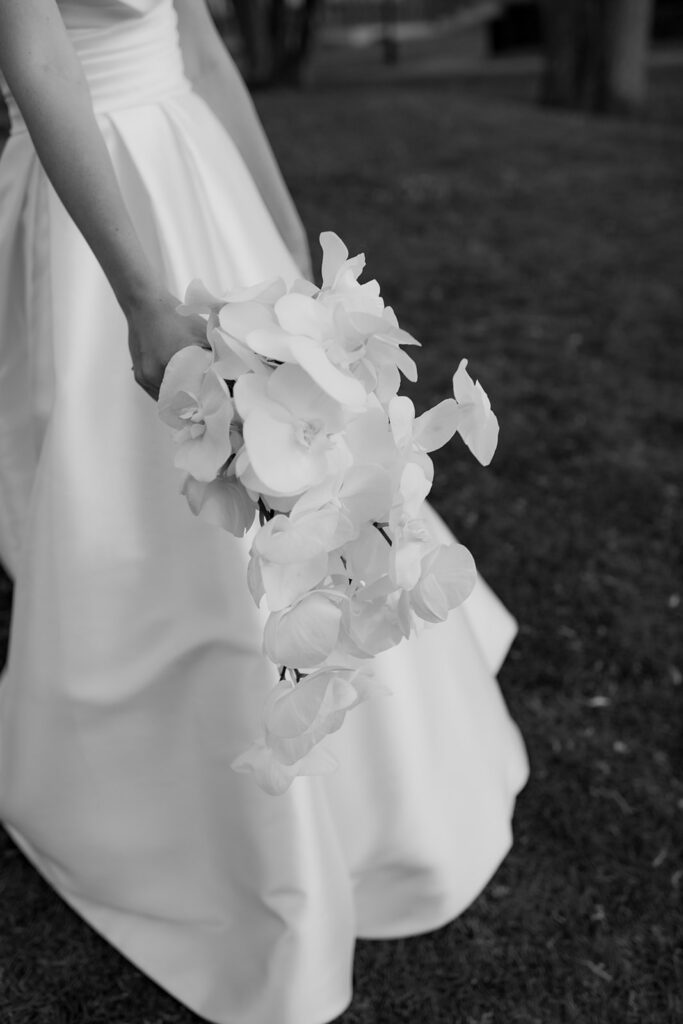 Wedding at Norrvikens trädgårdar 69 Black and white close-up of white orchids in a bouquet held against the wedding dress