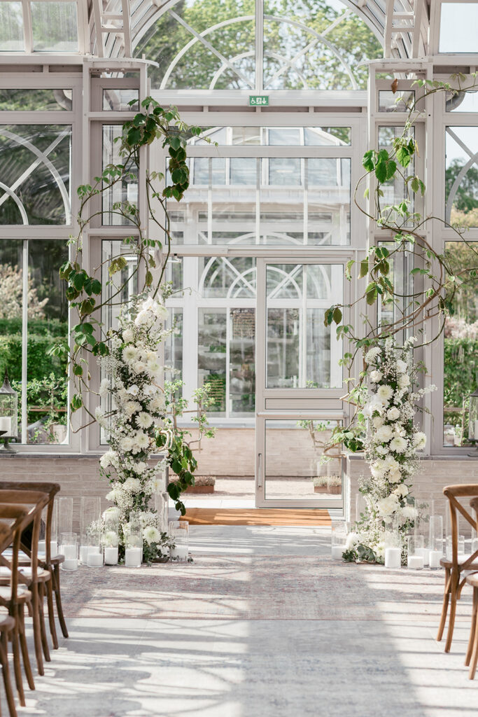 Wedding at Norrvikens trädgårdar 46 The aisle in Victoriahuset framed by tall white floral arrangements and greenery