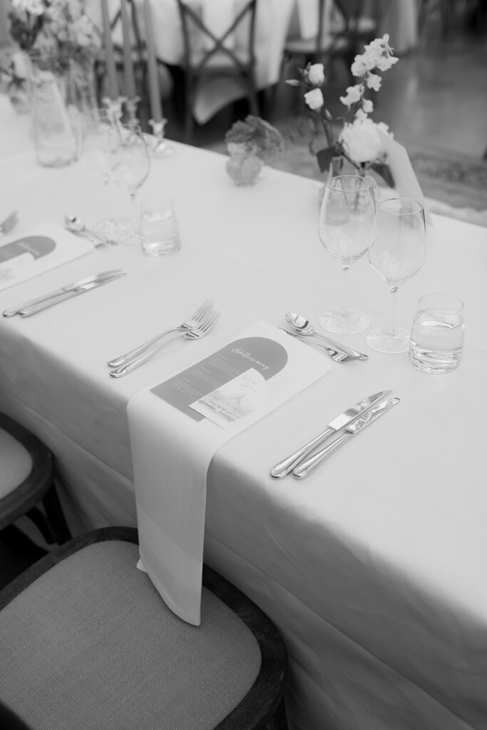 Wedding at Norrvikens trädgårdar 58 Black and white: table setting with folded napkin, cutlery and glasses on a white tablecloth