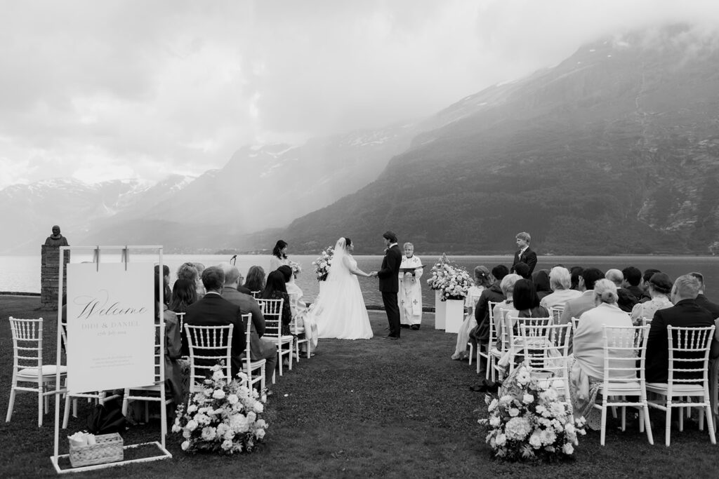 Utomhusvigsel vid fjord och berg i svartvitt med gäster på vita stolar
