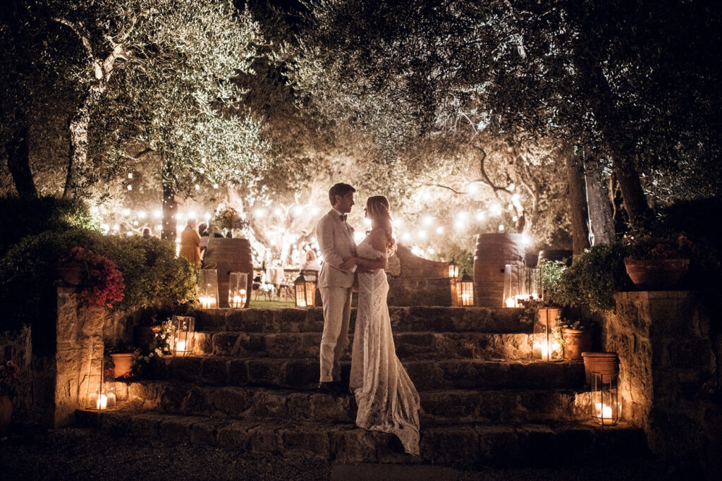 Evening wedding reception with string lights and candles under trees, Tuscany