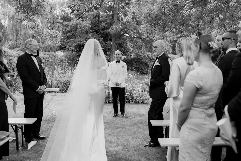 Wedding at Jordberga: a photographer's guide 14 Bride walking down the aisle in a long veil as guests stand, black and white