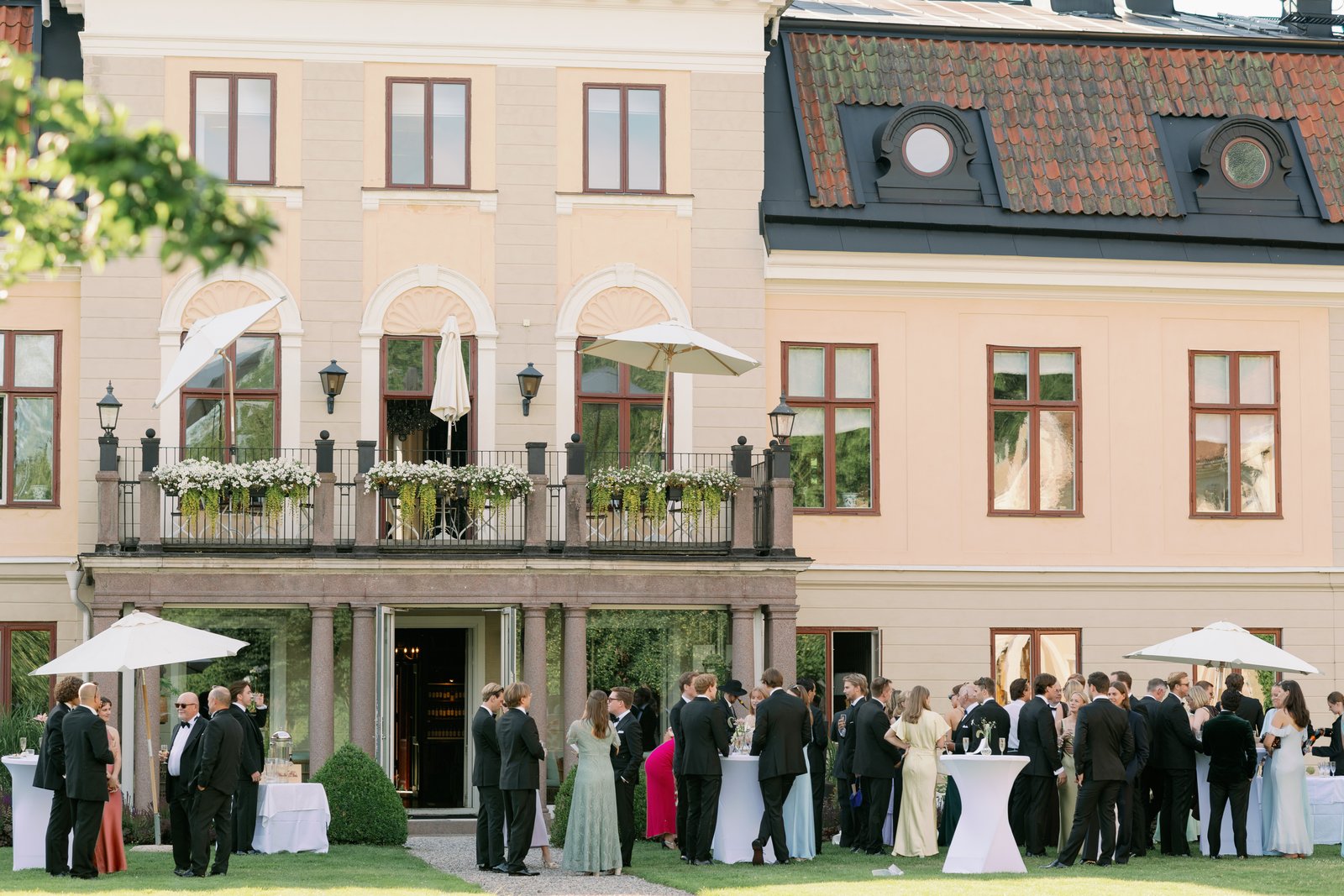Wedding guests gathered on the lawn in front of a pale manor house