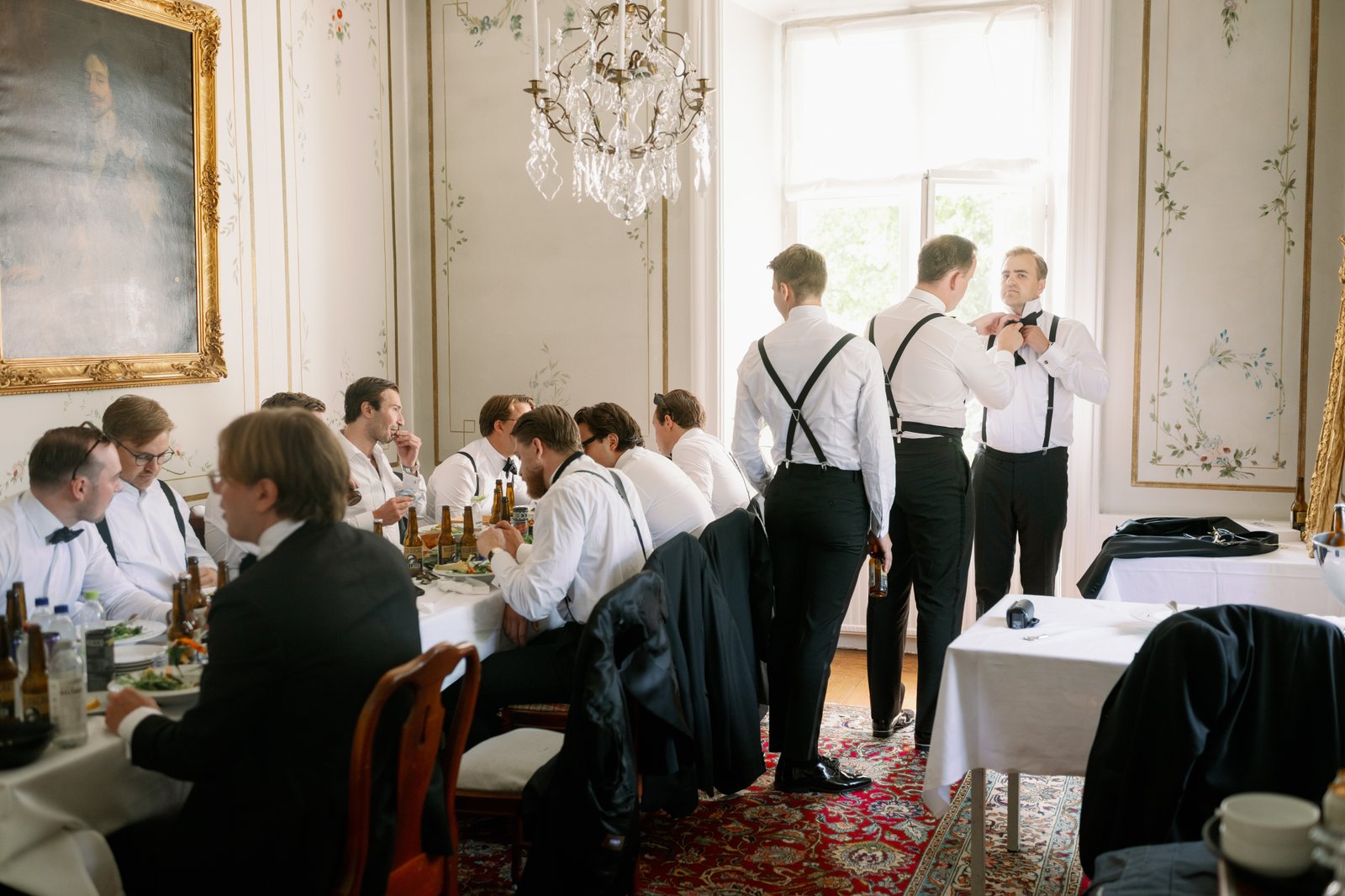 The groom and his party getting ready in a room with tall windows
