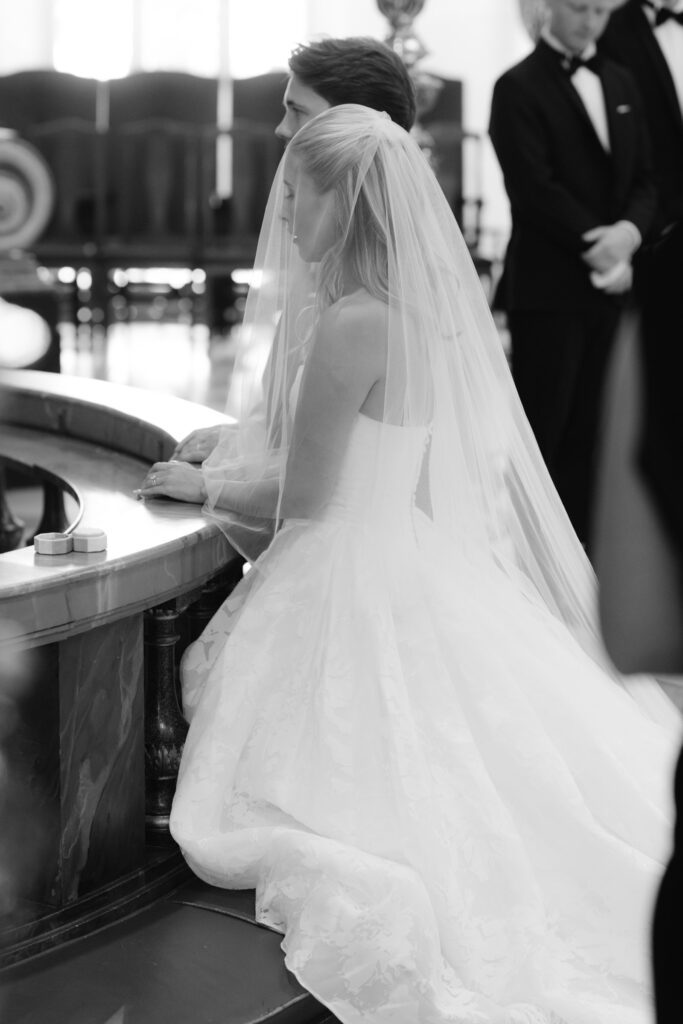 Wedding at Hasselbacken: a photographer's guide 21 Couple kneeling at the altar rail during the ceremony, the veil over the bride’s shoulders, black and white