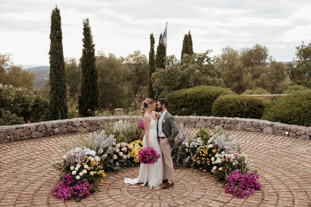 Bride and groom facing each other on the round stone ceremony terrace at Millstone Villa, Kefalonia, with flowers around them