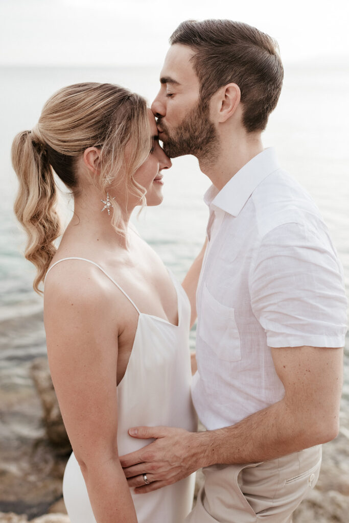 Groom kissing the bride on the forehead at the water on Kefalonia