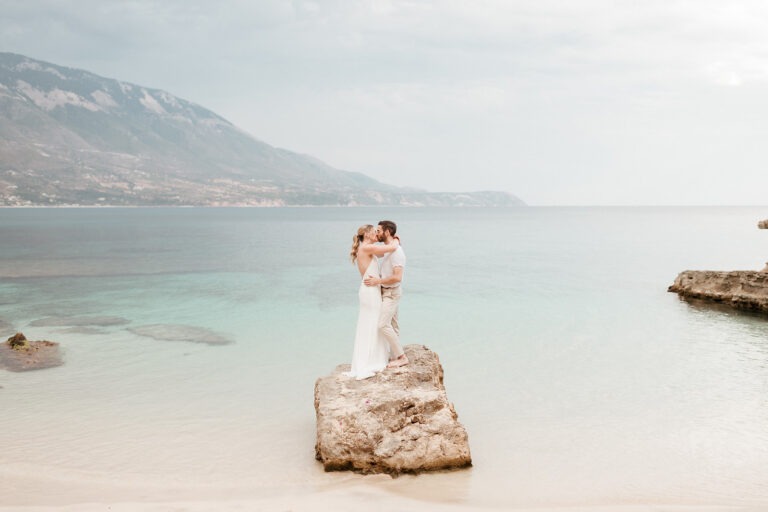 Wedding photographer Greece: bride and groom kissing on a rock in shallow turquoise water on Kefalonia