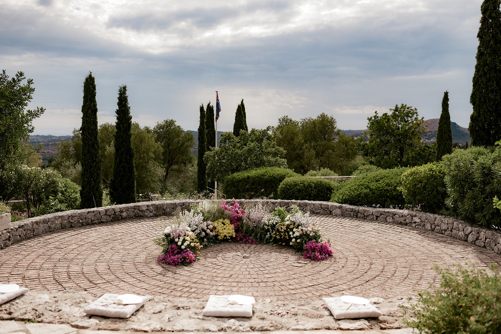 Round stone ceremony terrace with cypresses and a half circle of flowers at Millstone Villa, Kefalonia, before the guests arrive