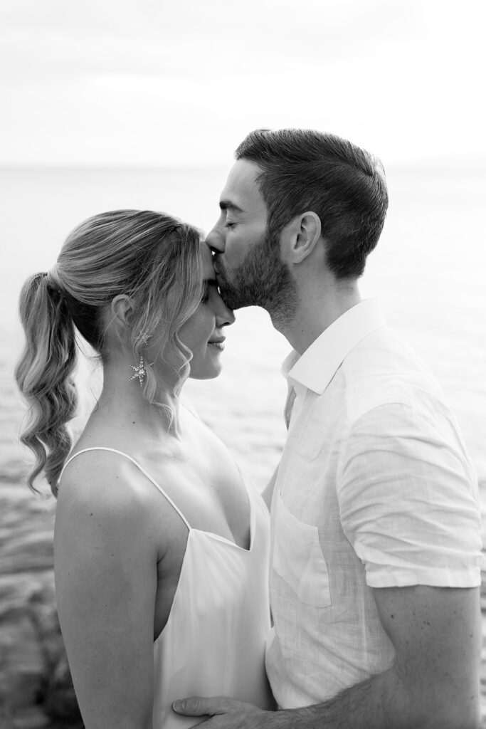 Groom kissing the bride on the forehead by the sea on Kefalonia, black and white