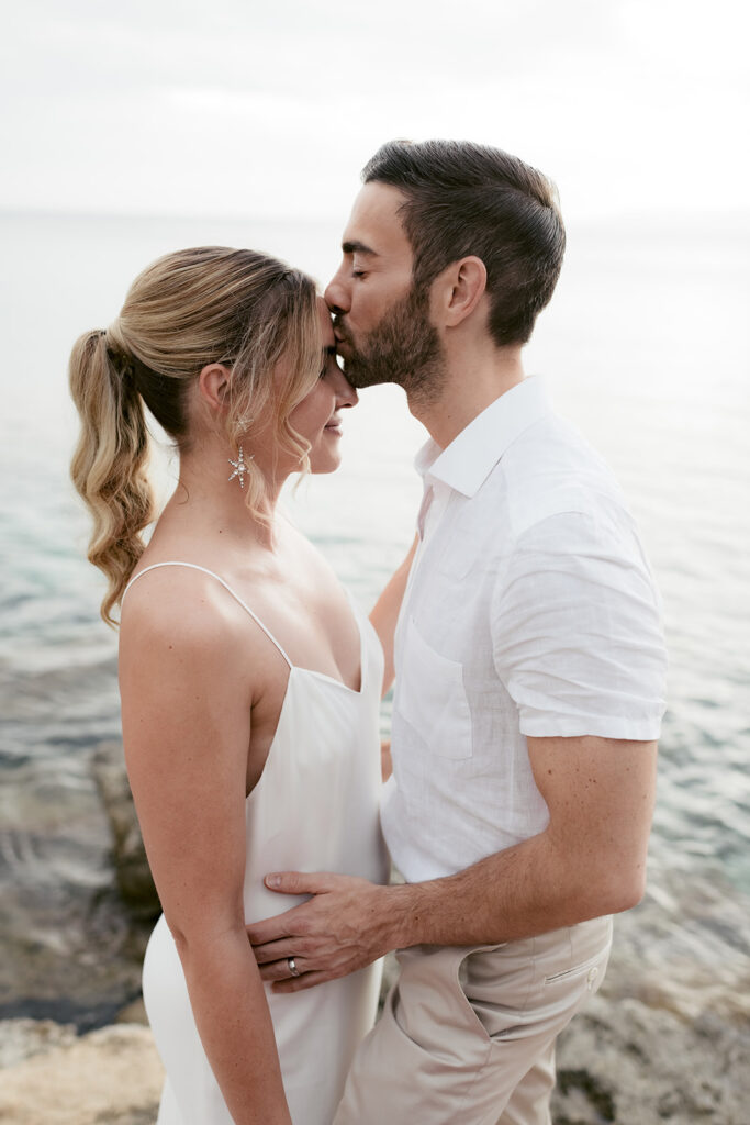 Wedding couple at the shore on Kefalonia, groom kissing the bride on the temple