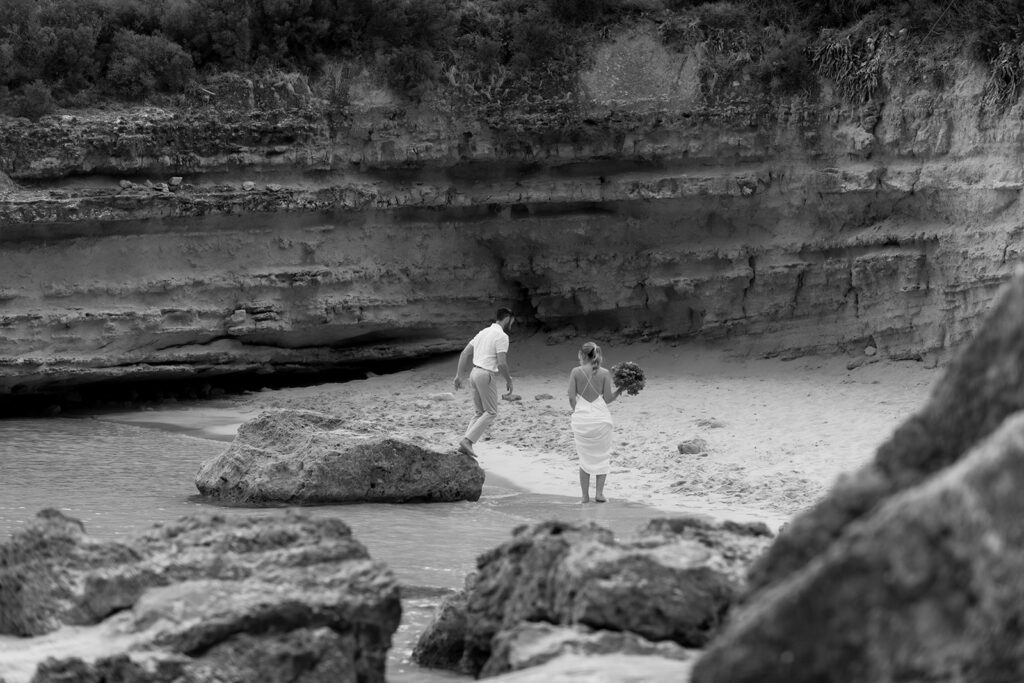 Wedding couple on the beach seen between rocks and cliff on Kefalonia, black and white