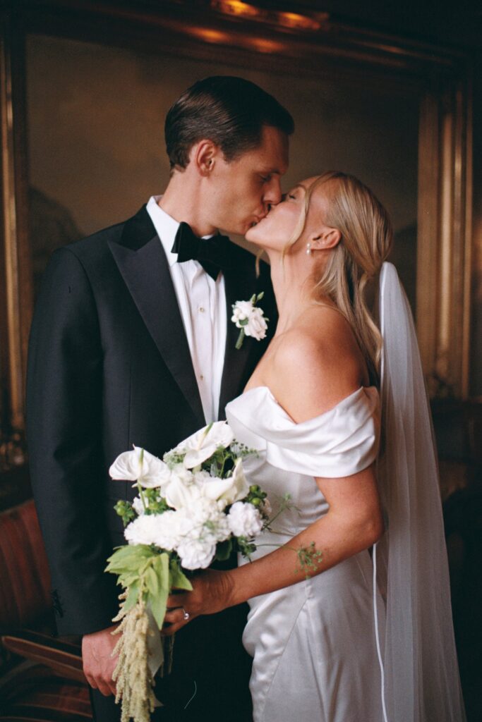 Wedding at Thorskogs Slott 28 The couple kisses indoors in warm light, the bride holding a white bouquet, shot on 35mm film