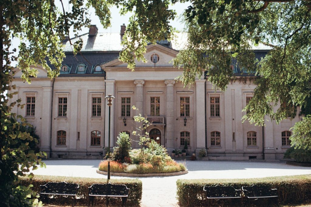 The front of the castle with its entrance and a planted roundabout, seen between the trees, shot on 35mm film