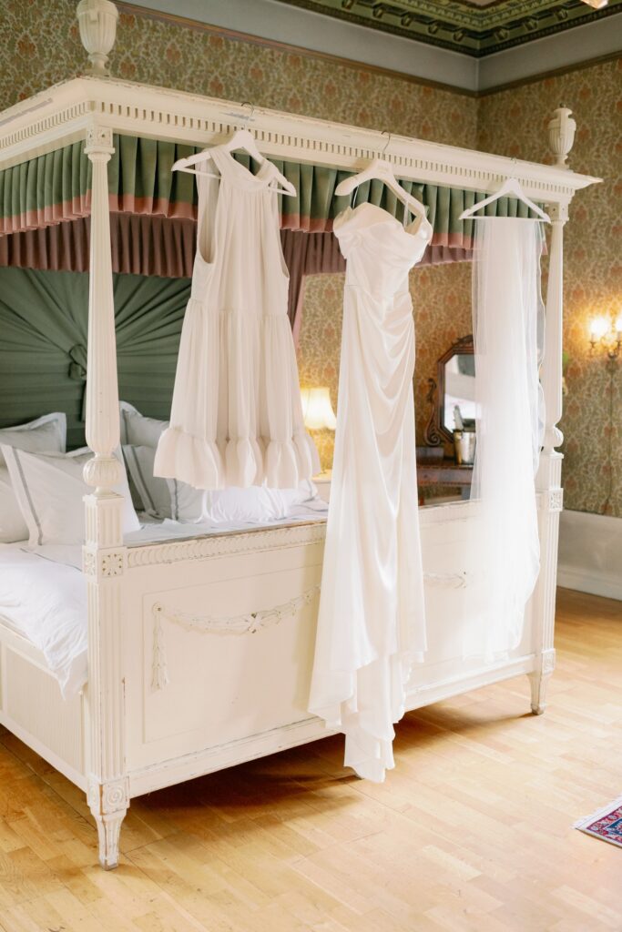 Wedding at Thorskogs Slott 15 Two dresses and a veil hang from a four-poster bed in a room with green drapes