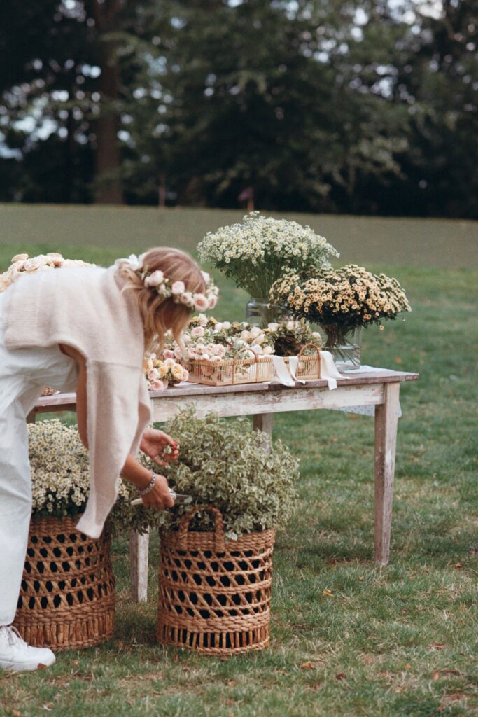 A woman arranges flowers in woven baskets by a wooden table on the lawn, shot on 35mm film