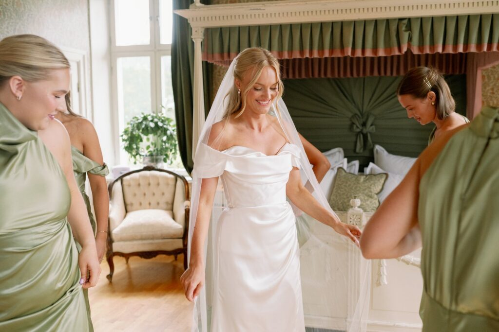 Wedding at Thorskogs Slott 14 Bridesmaids in green help the bride with her dress by the four-poster bed