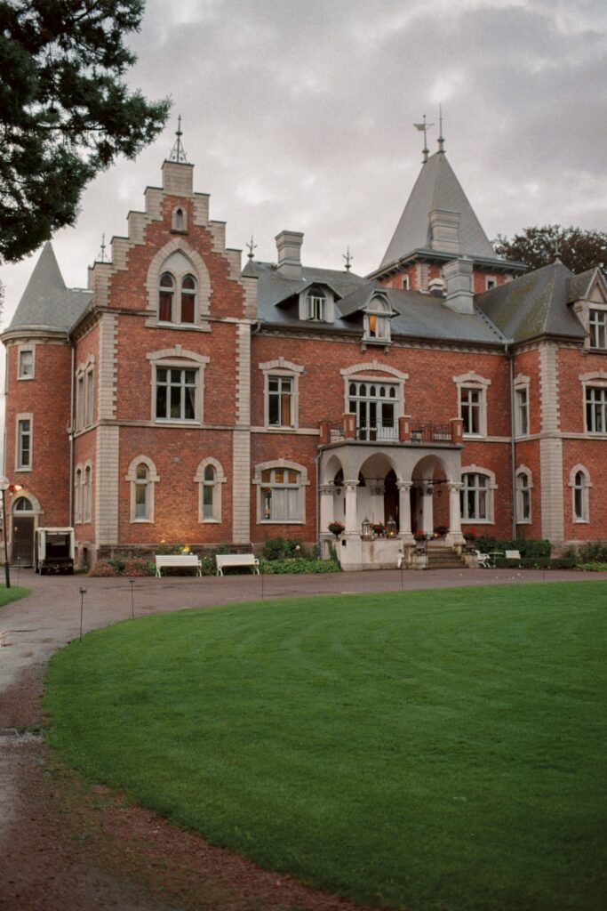 Wedding at Thorskogs Slott 13 The castle facade with stepped gables and a turret under a cloudy sky, the lawn in front, shot on 35mm film