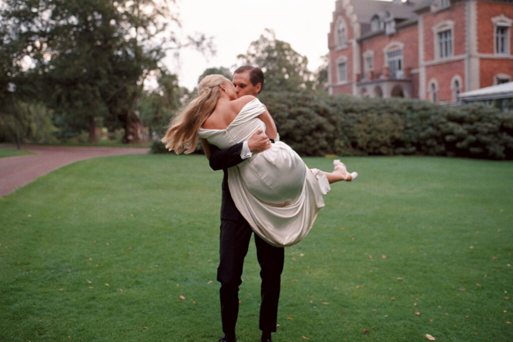 Wedding at Thorskogs Slott 36 The groom carries the bride across the lawn, the castle behind them, shot on 35mm film
