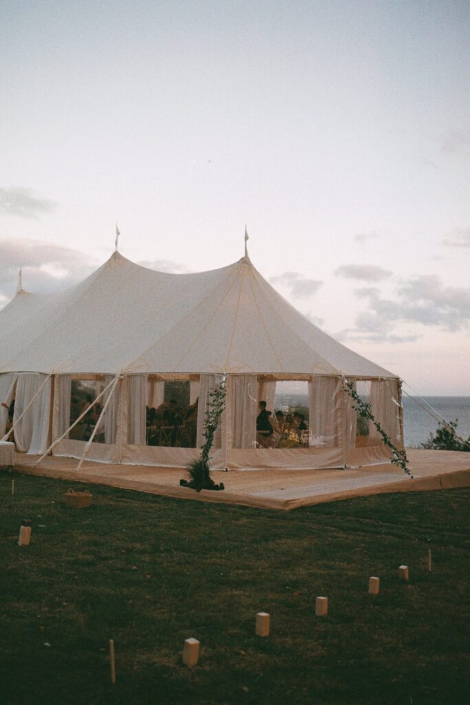 White marquee on the lawn at dusk with the sea behind and lanterns in the grass, shot on 35mm film