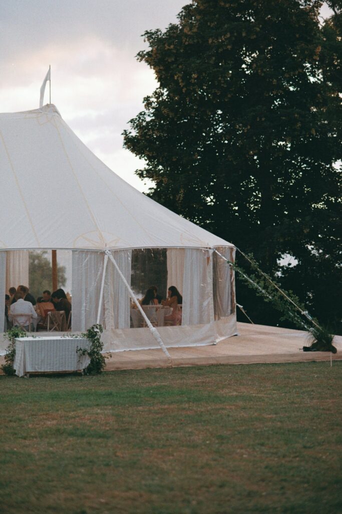 Guests at the tables inside the white marquee among the trees, shot on 35mm film