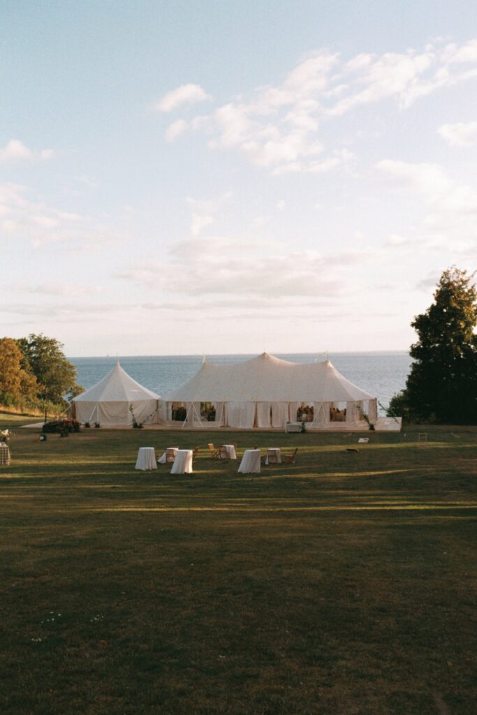 The marquees on the lawn with the Öresund strait and horizon behind, white standing tables spread across the grass, shot on 35mm film