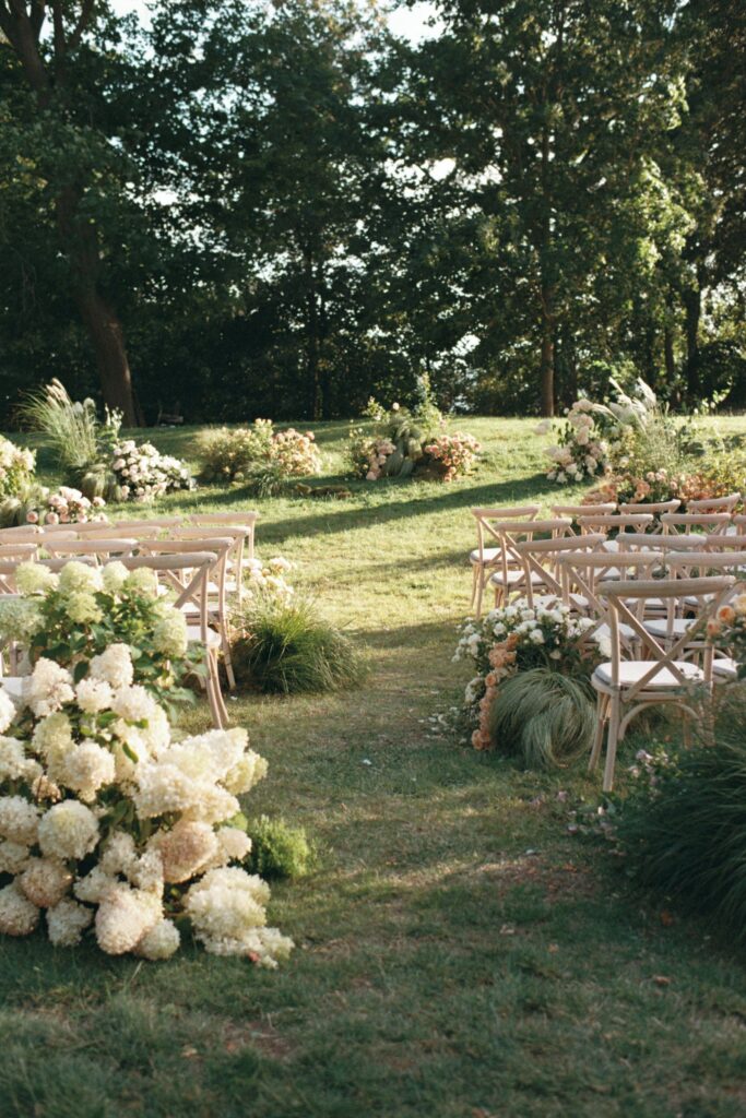 The aisle between wooden chairs with white hydrangeas in the foreground, shot on 35mm film