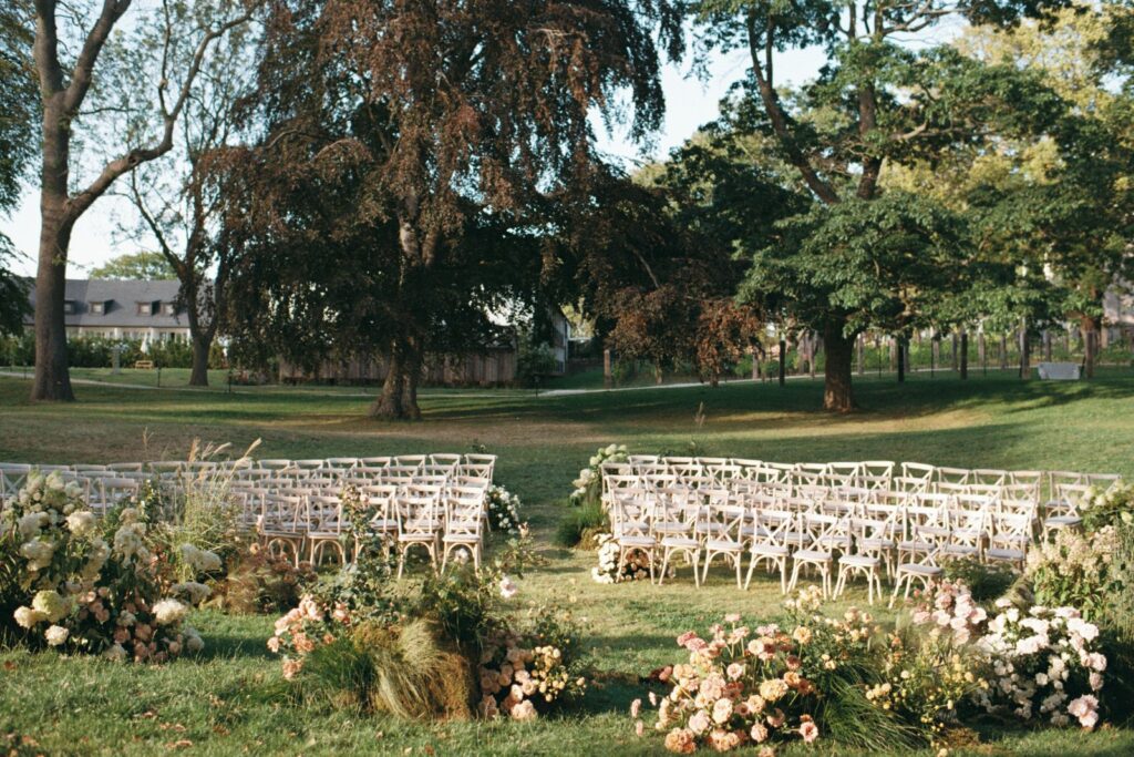 The ceremony space with two blocks of chairs and floral arrangements under large trees, shot on 35mm film