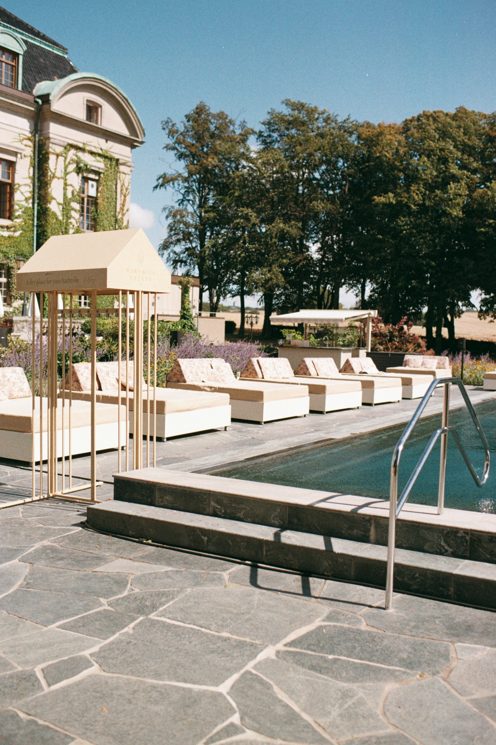 Pool with sun loungers and a pavilion in sunshine beside the castle building, shot on 35mm film