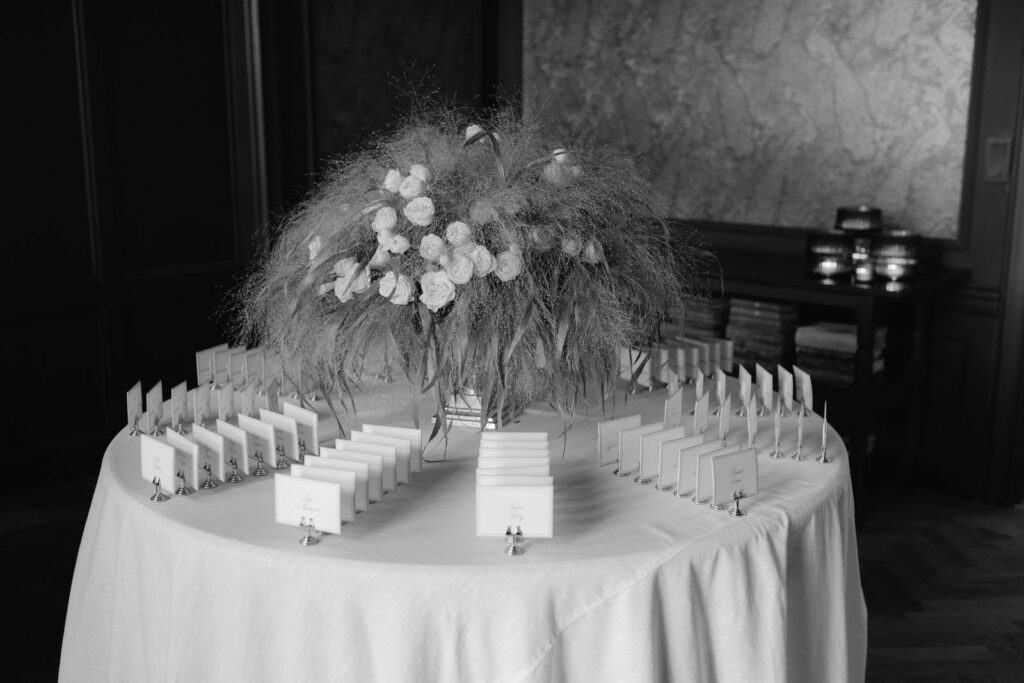Bröllop på Villa Fridhem: en fotografs guide 22 Svartvitt: bordsplaceringskort på ett runt bord under en stor blomsteruppsättning