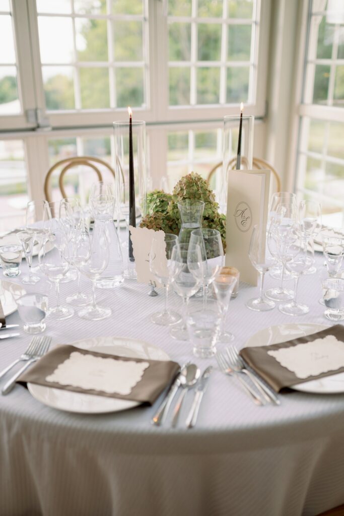 Round table with glasses, plates with brown napkins and menu cards
