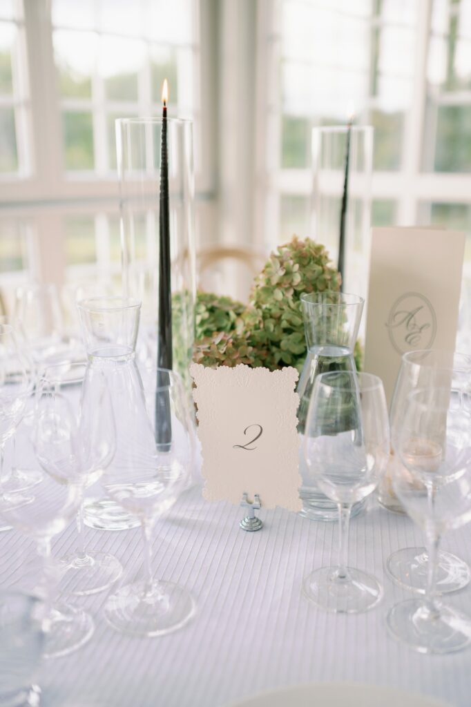 Table setting with glasses, a black candle and table number two among green flowers