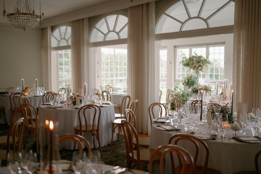 Dining room with arched windows, a chandelier and round tables set for dinner