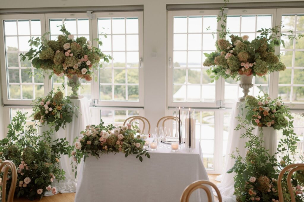 Long table with tall floral arrangements in front of paned windows
