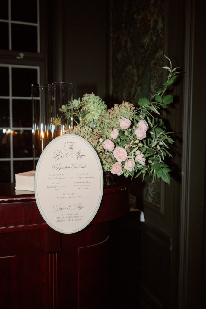 Bröllop på Villa Fridhem: en fotografs guide 7 Välkomstskylt på ett staffli bredvid rosa och gröna blommor i en mörk hall