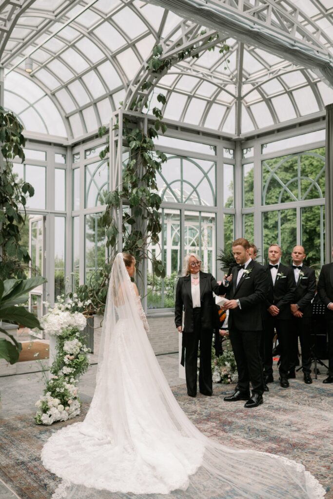 Wedding at Norrvikens trädgårdar 25 Ceremony in Victoriahuset, the bride in a long veil facing the groom and the officiant