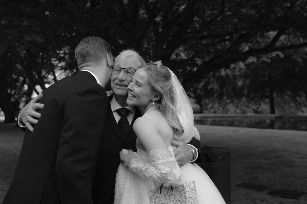 Wedding at Norrvikens trädgårdar 32 Black and white: an older man hugging the couple