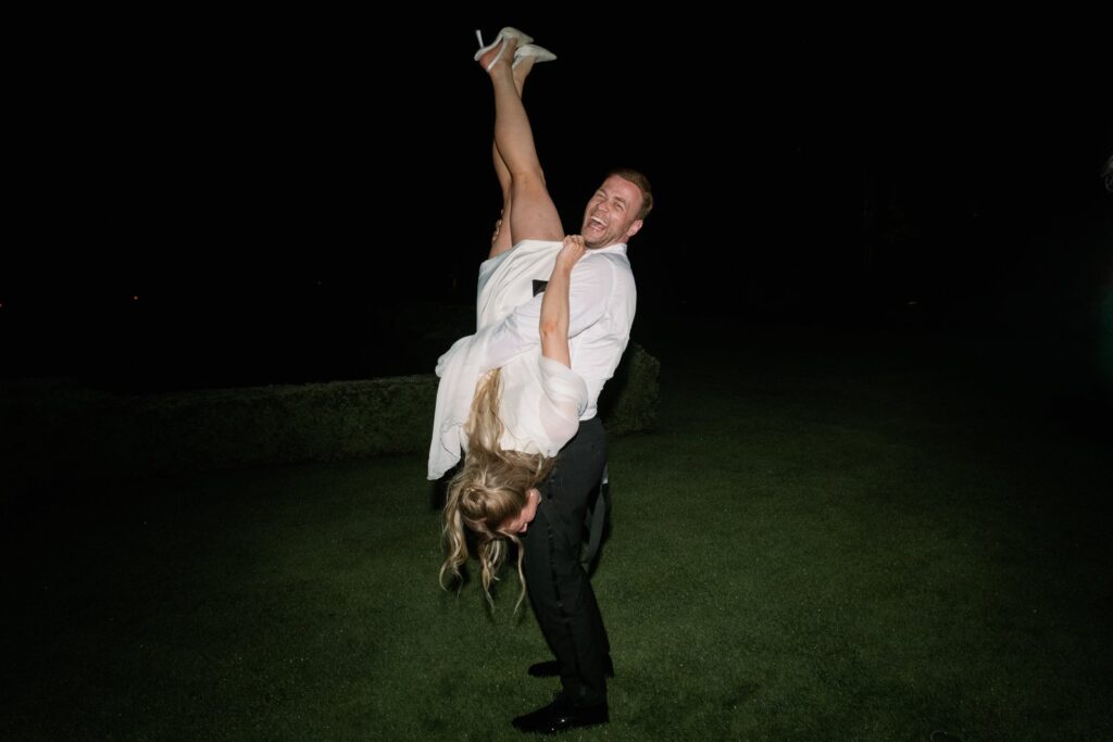 Wedding at Norrvikens trädgårdar 19 The groom lifts the bride upside down on the lawn after dark, lit by flash