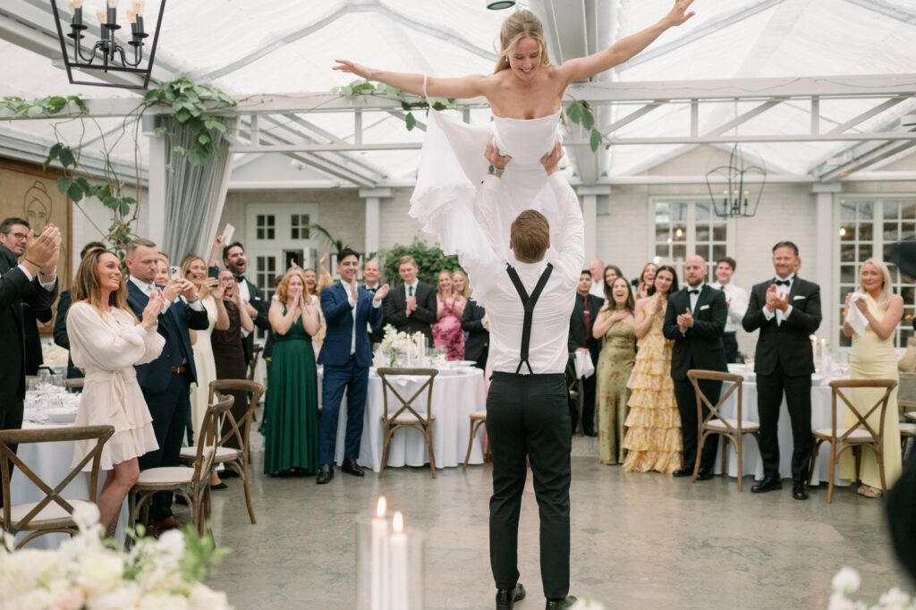 Wedding at Norrvikens trädgårdar 11 The groom lifts the bride high under the glass roof as guests cheer around the dance floor