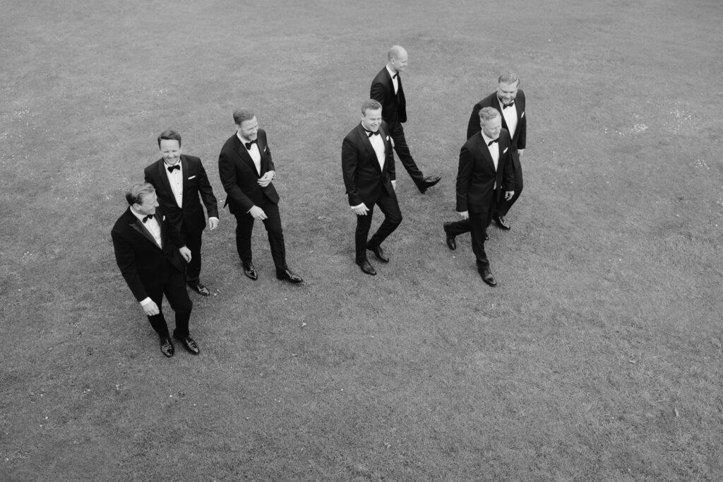 Wedding at Norrvikens trädgårdar 10 Black and white from above: a group of men in tuxedos walking across the lawn