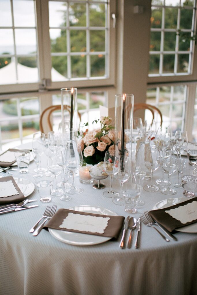 Close-up of a set table with crystal glasses, roses and tall candlesticks by the window, shot on 35mm film