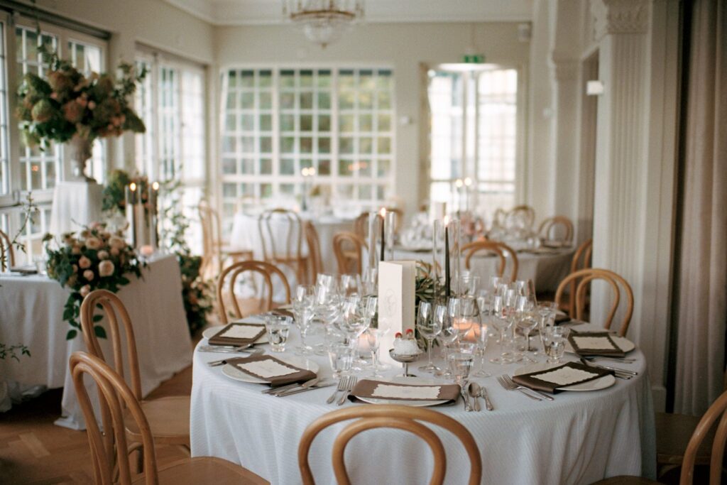 Round tables set in a bright dining room with paned windows and a chandelier, shot on 35mm film