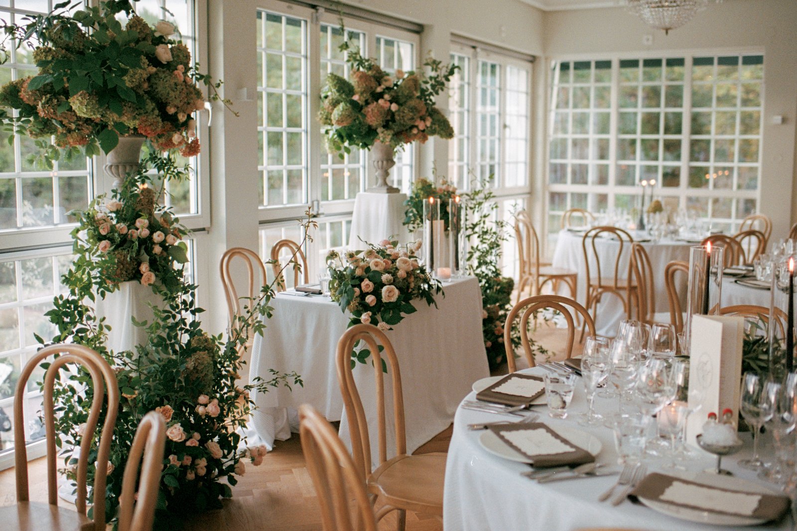 Bröllop på Villa Fridhem: en fotografs guide 2 Matsalen med runda bord och en hög blomsterpelare vid fönstren, fotograferat på analog 35 mm-film
